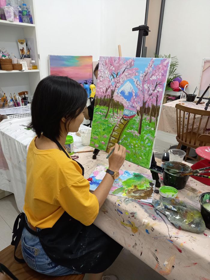 Home Woman in yellow shirt paints cherry blossom scene on canvas in a workshop.