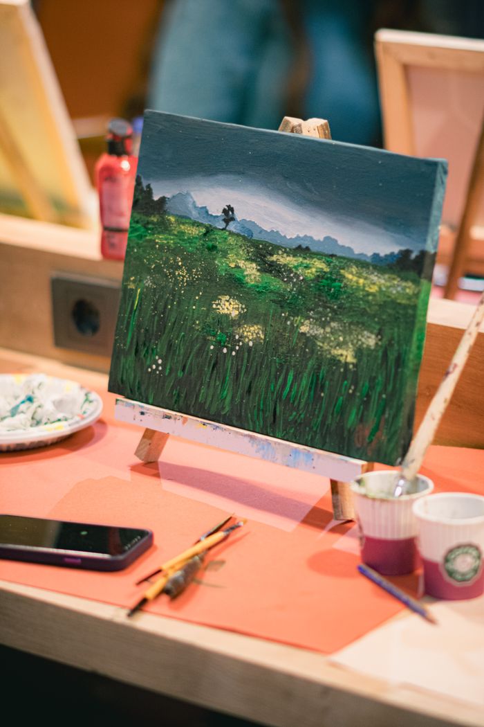 Home Close-up view of artistic landscape painting on easel surrounded by paintbrushes and a smartphone.