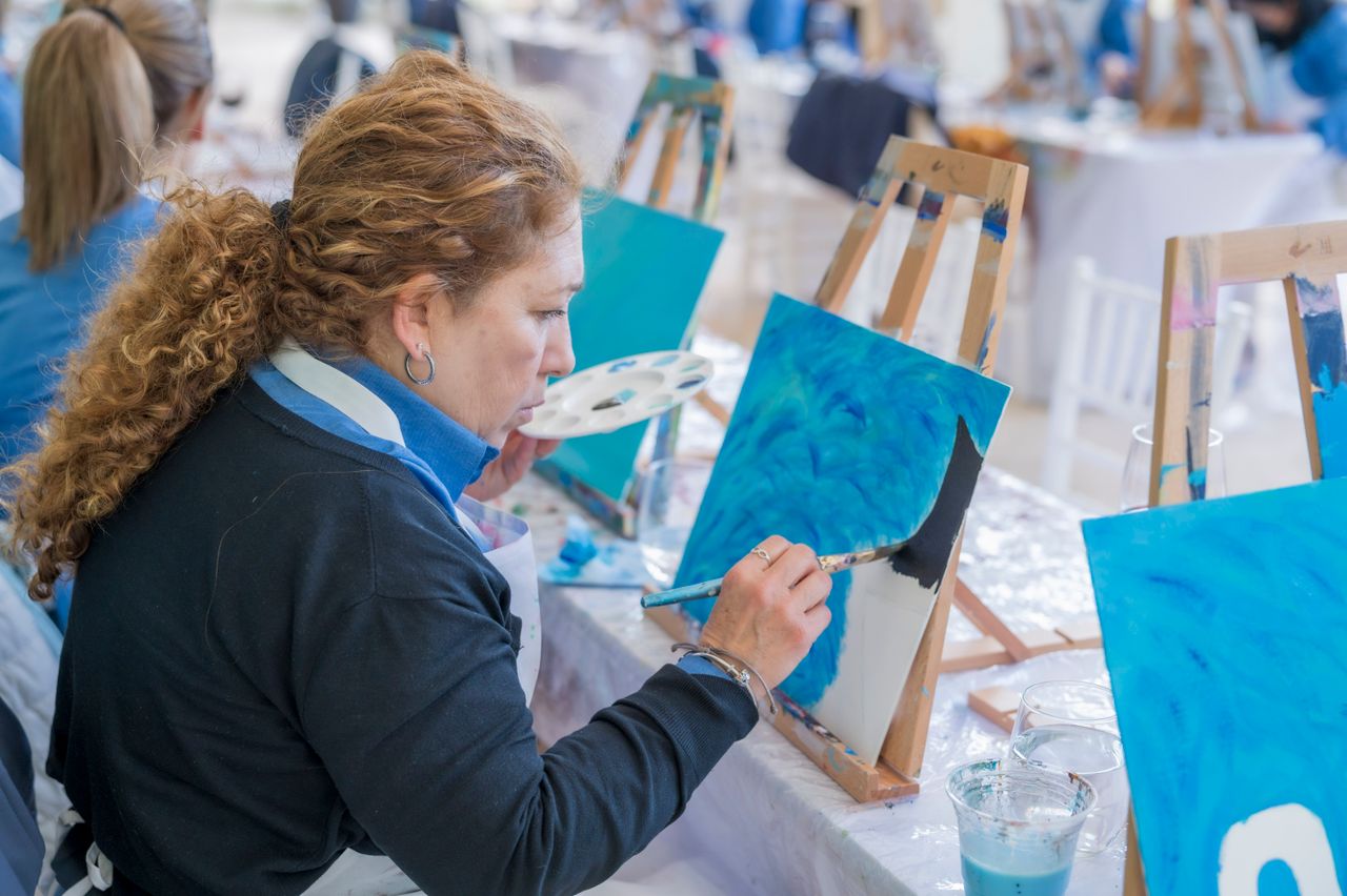 Home An adult woman engaged in a painting session at an art workshop with easels and paint.