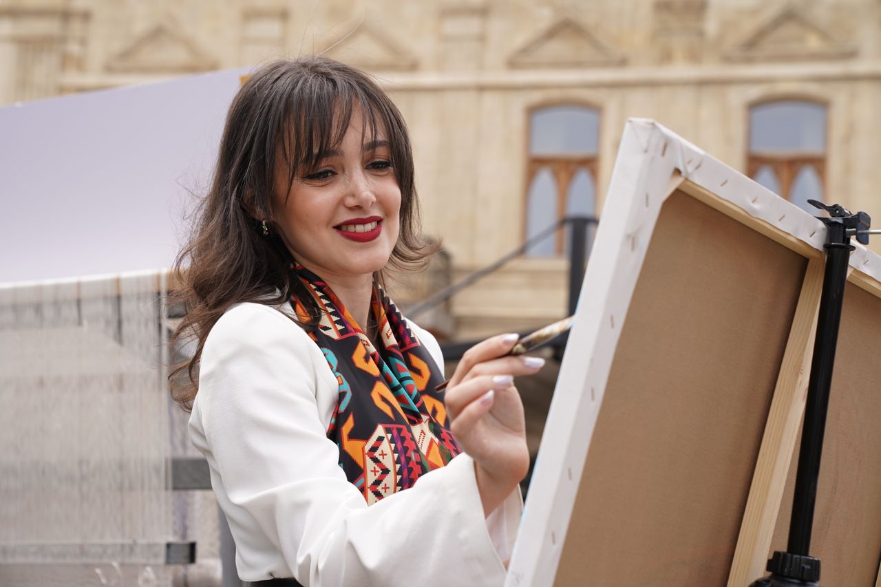 Home A female artist painting outdoors in Baku, showcasing creativity and art in a cultural setting.