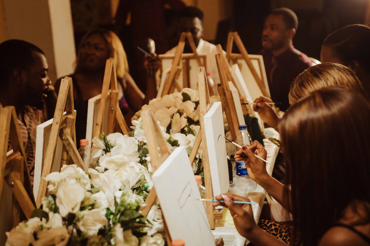 Home A group of adults engaged in a fun painting session with easels and flowers, captured indoors.