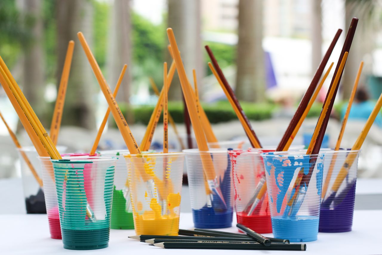Offerings Vibrant paint brushes and pencils in plastic cups for arts and crafts.