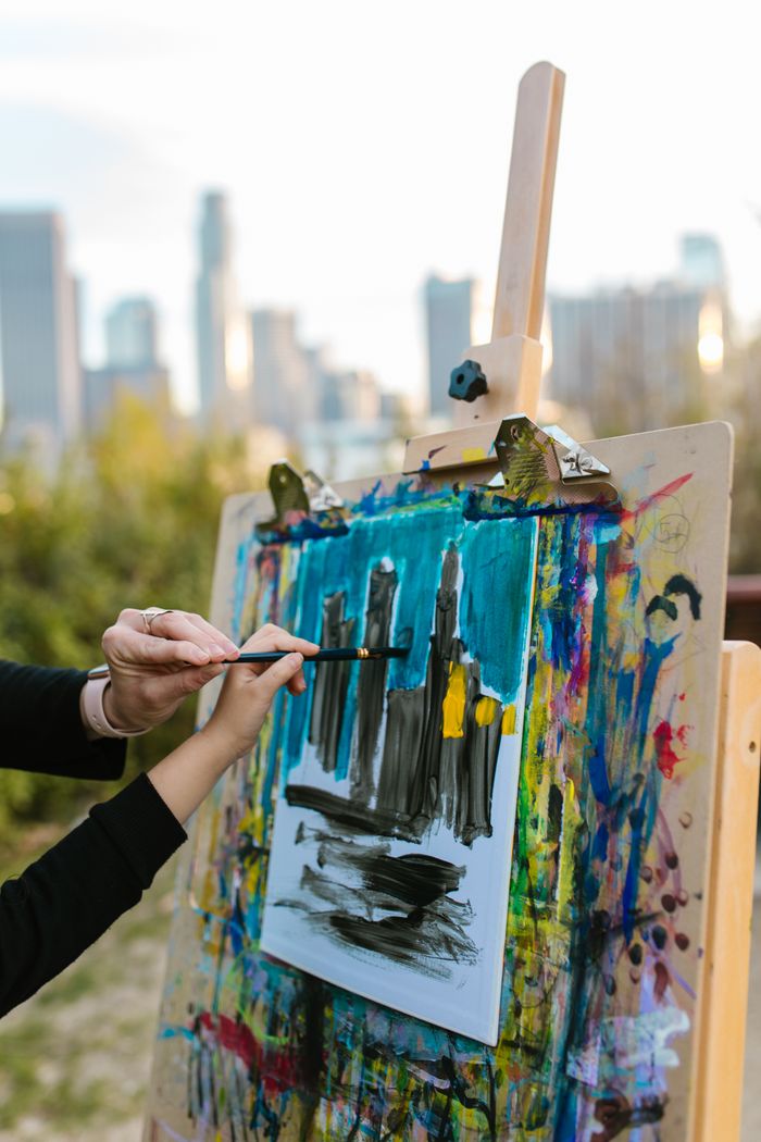 Home Artist painting city skyline on easel outdoors. Vibrant colors and creative expression.