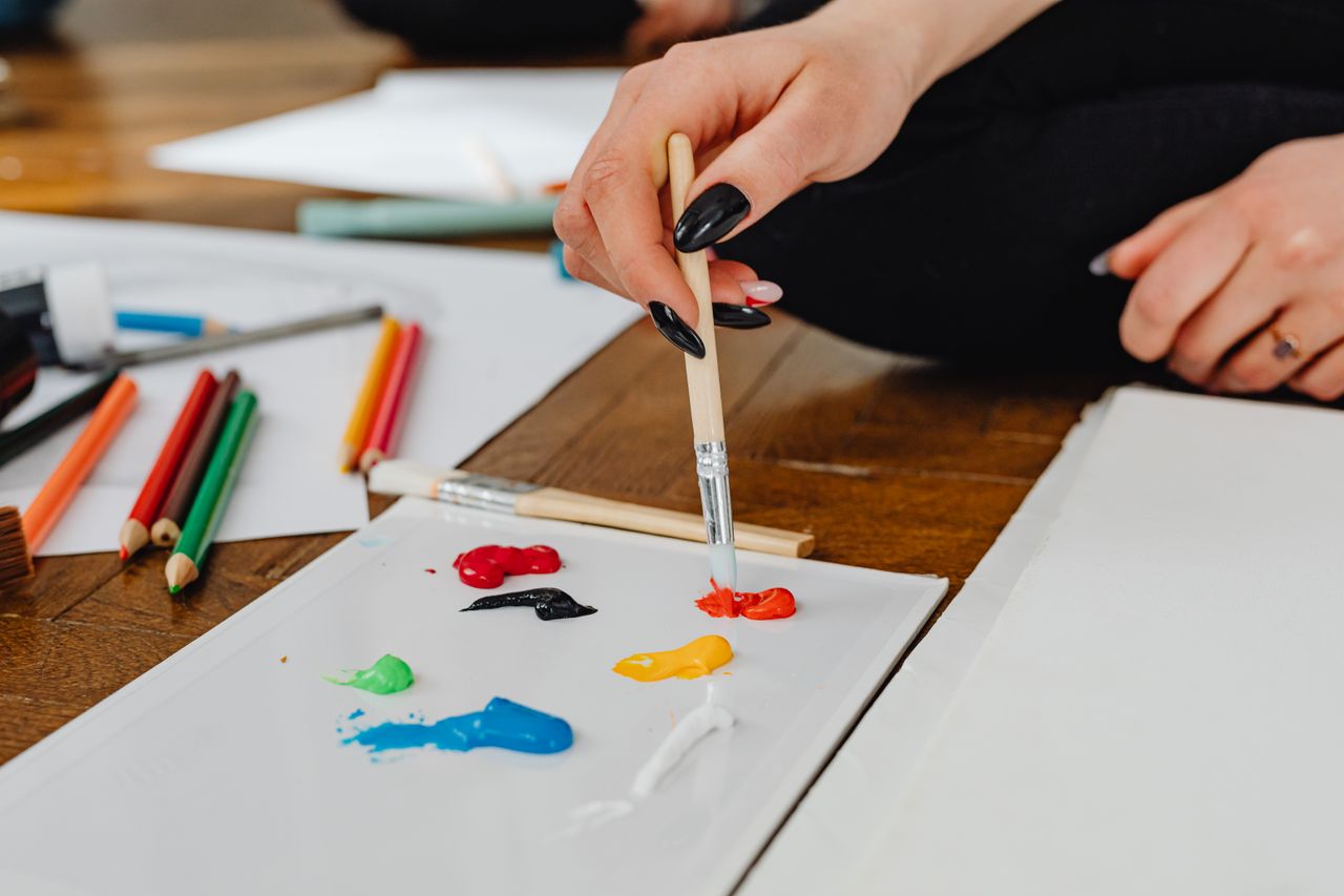 Hand using a paintbrush to mix colorful paints on a paper. Creative art scene.